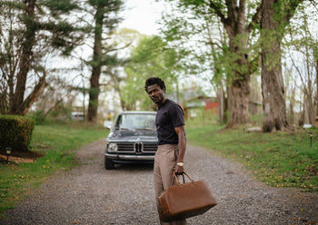 model holding weekend bag in front of old BMW