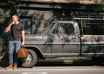 man holding leather duffle near truck