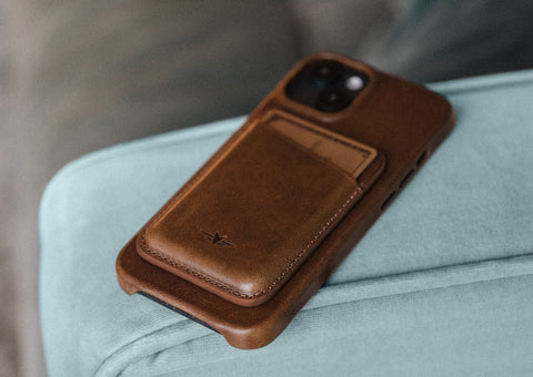 Brown Heirloom quality leather Magsafe wallet attached to leather iPhone case laying on arm of chair