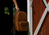 brown leather backpack in front of barn