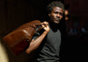 man holding brown leather weekend bag by handles