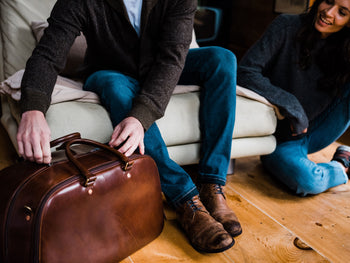 man opening brown leather zippered duffle bag