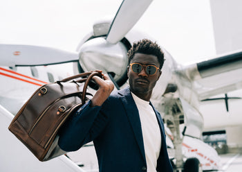 man carrying brown leather carry on bag outside of plane
