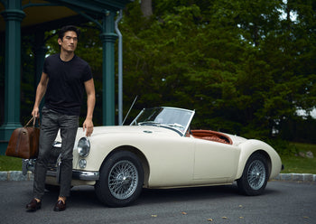 well dressed man carrying travel bag next to vintage car