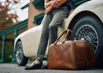 smooth brown leather travel bag next to vintage car
