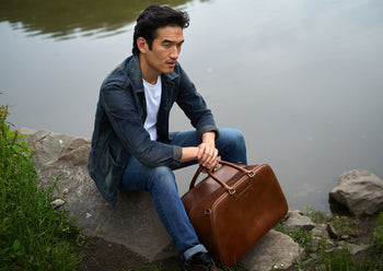 man holding brown leather weekender by handles